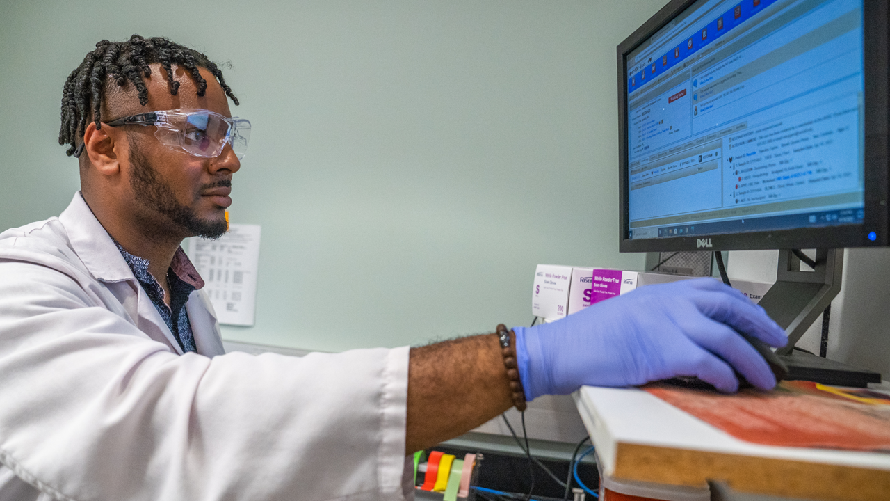 A young man in lab coat and gloves examining a file on a computer