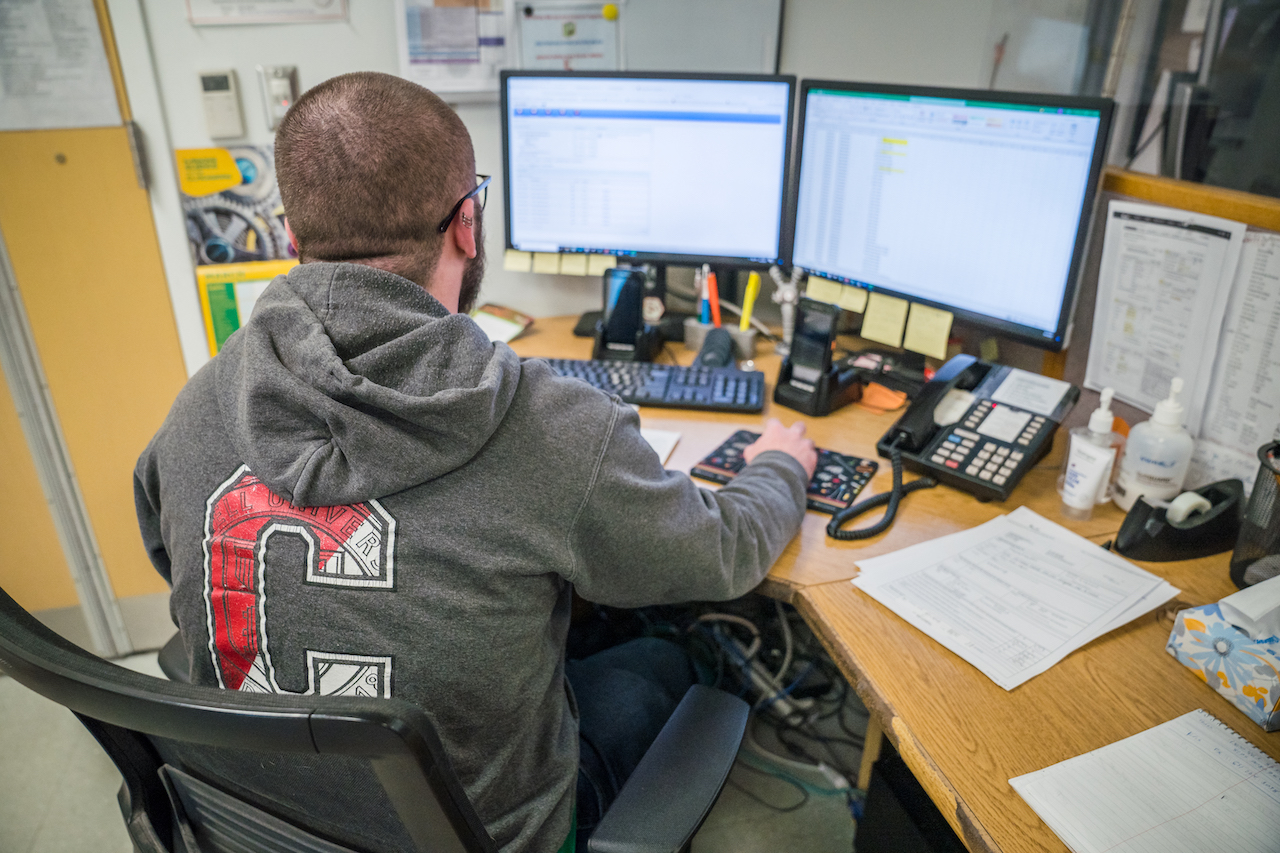 The back of a man in a Cornell sweatshirt examining a double monitor