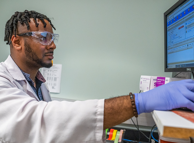A young man in lab coat and gloves examining a file on a computer