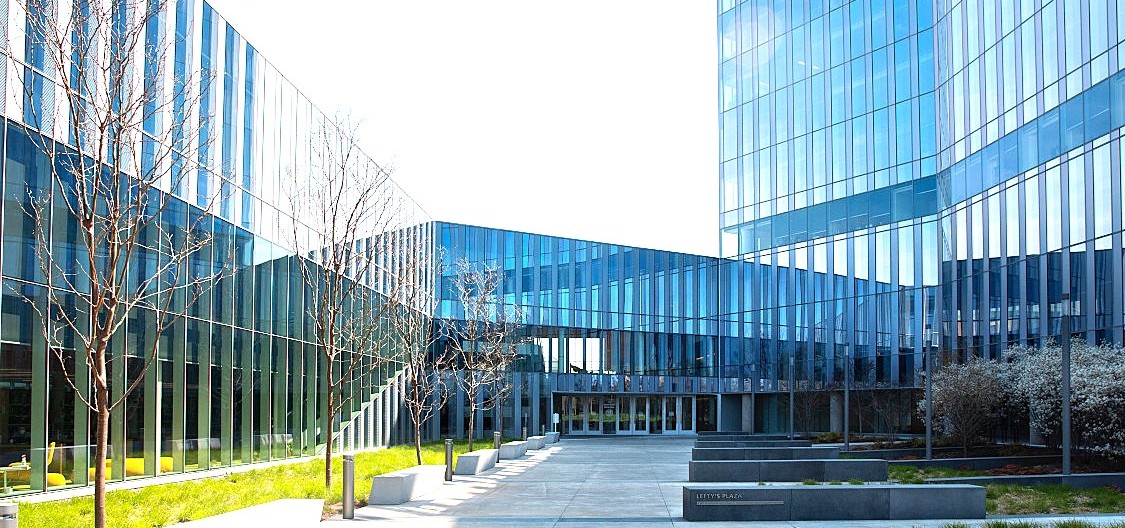 Glass-walled modern building surrounding an open courtyard with young trees.