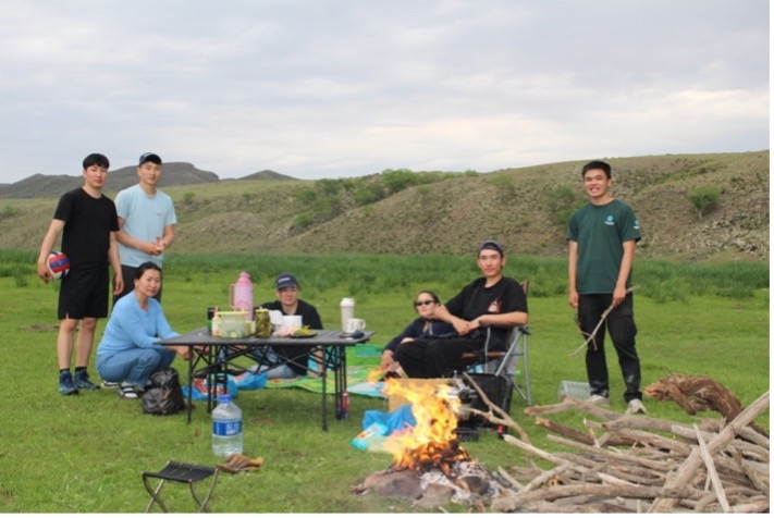 Nicholas Wang and Mongolian veterinary interns at a campsite that is green and hilly