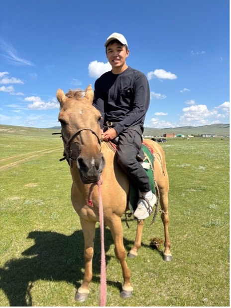 Nicholas Wang on a horse in a sunny Mongolian field