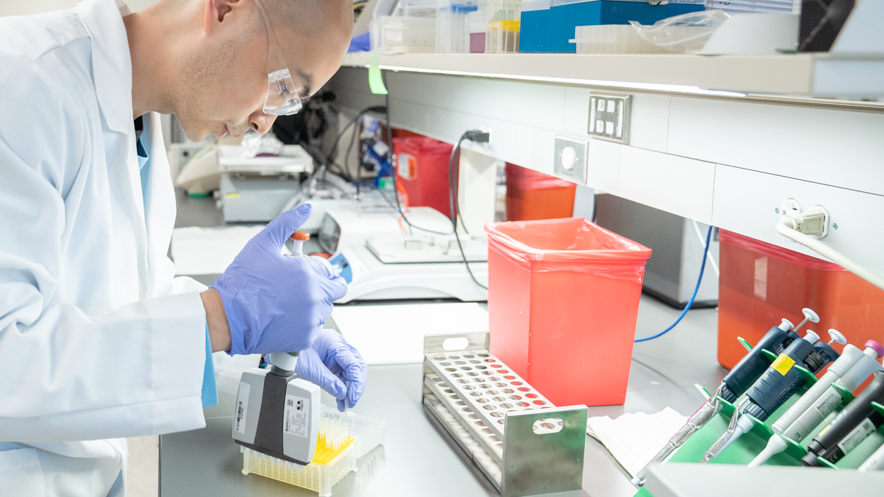 A man leans over a lab bench with a pipette