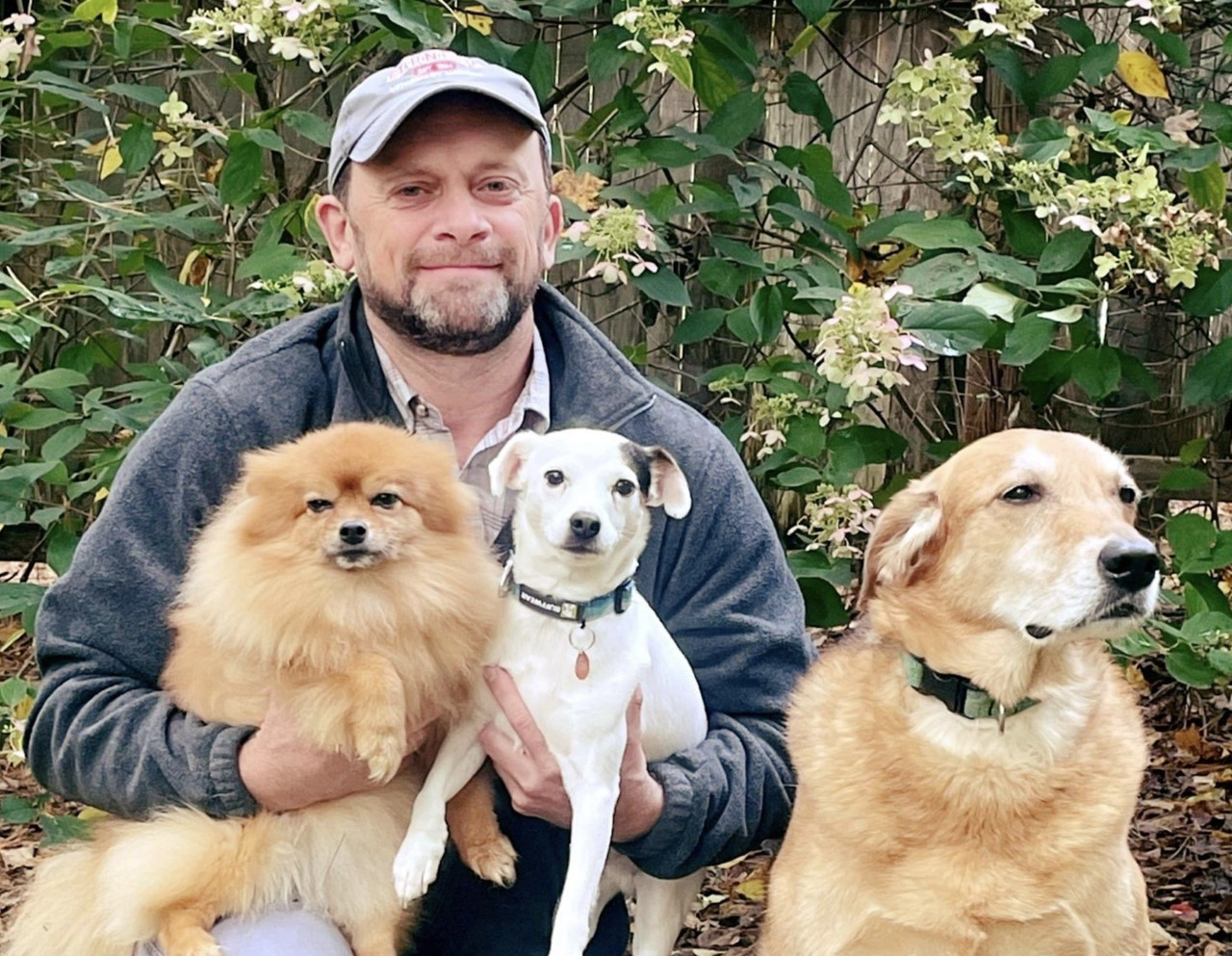 Dr. Brian Collins sits outside with three dogs