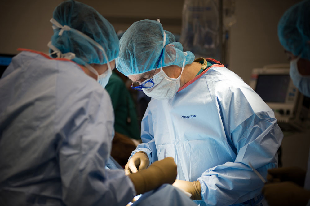 Norm Ducharme in surgery, wearing scrubs, a mask, hair cap, gloves