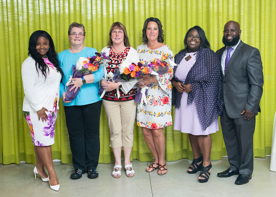 The recipients of the Dionne Henderson Staff Excellence Award pose with flowers in front of a green curtain with Henderson's family
