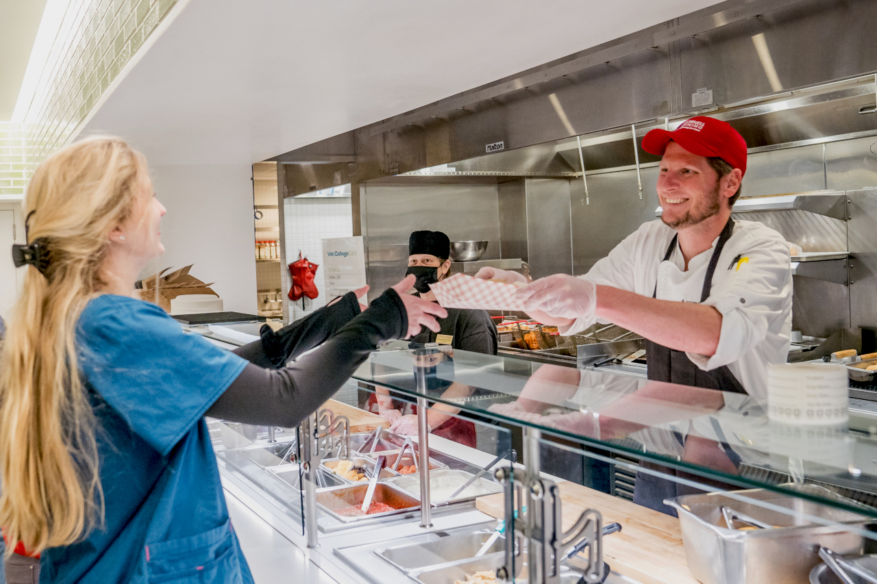 Cornell dining employee serving a plate of hot food to a DVM student