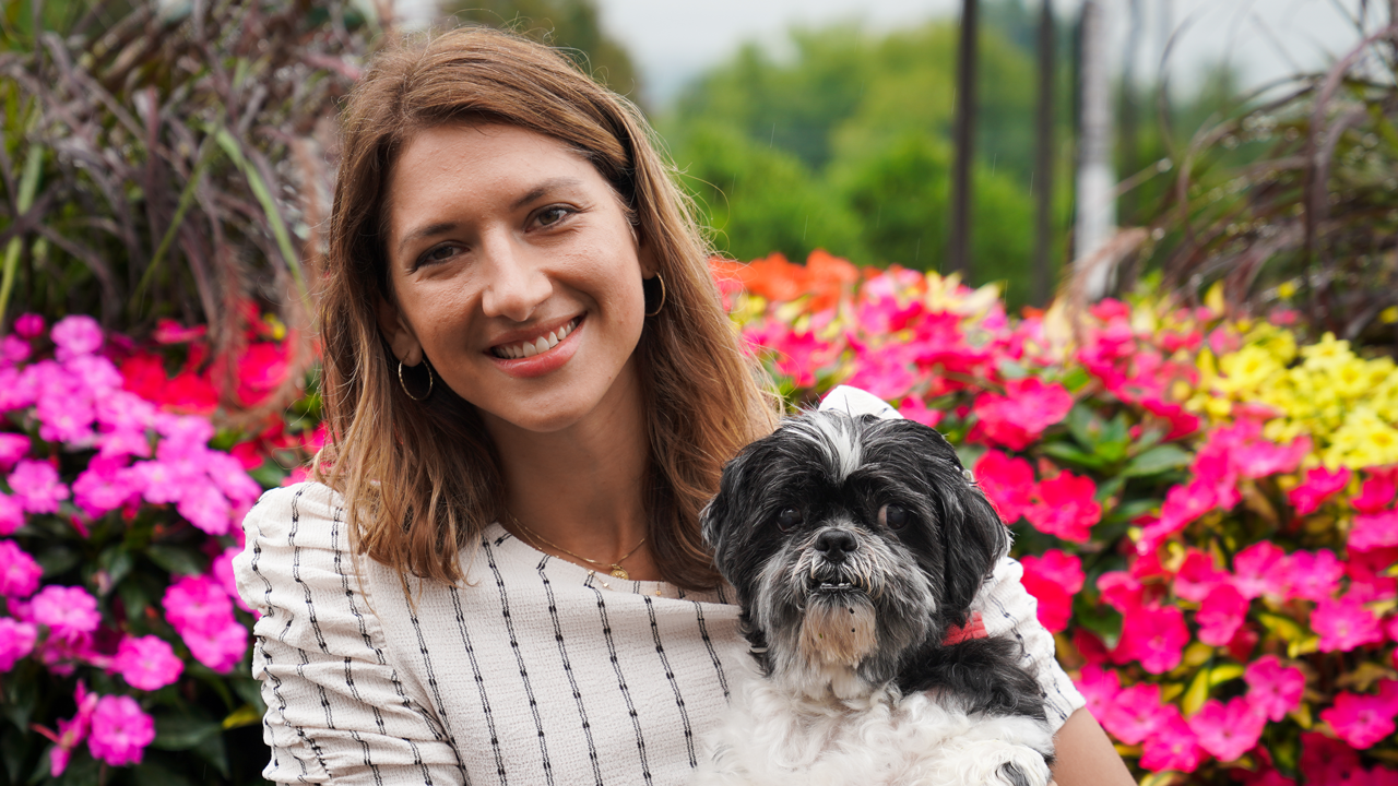 Stephanie Coco with a fluffy white dog seated outdoors near flowering bushes