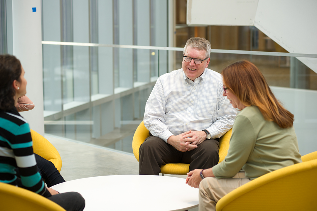 Dean Warnick talking with others in yellow atrium chairs