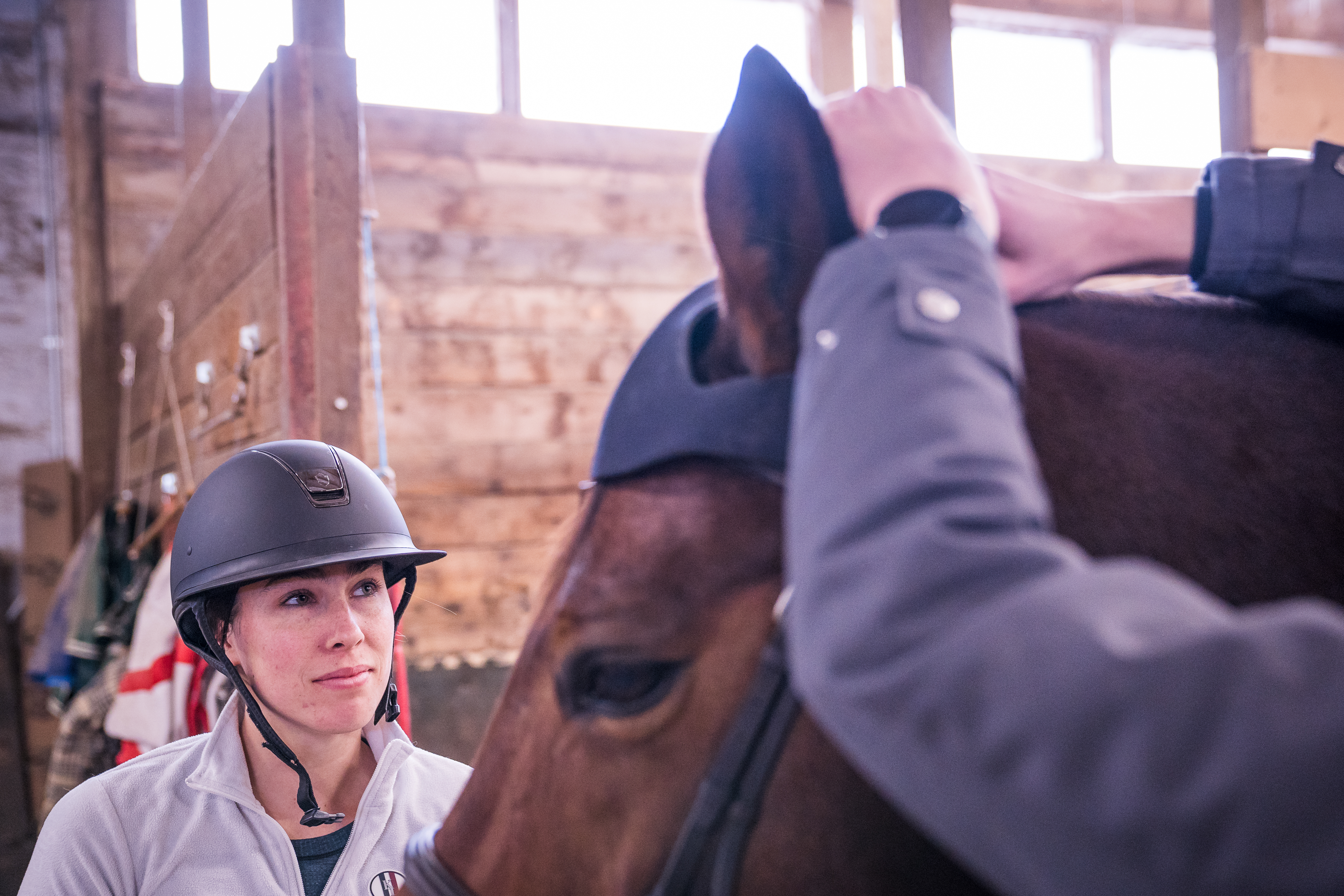 A rider looks on as a cap is placed on her horses head. 