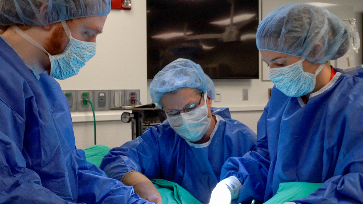 Fubini leading two students, all wearing scrubs, gloves, hair caps and masks