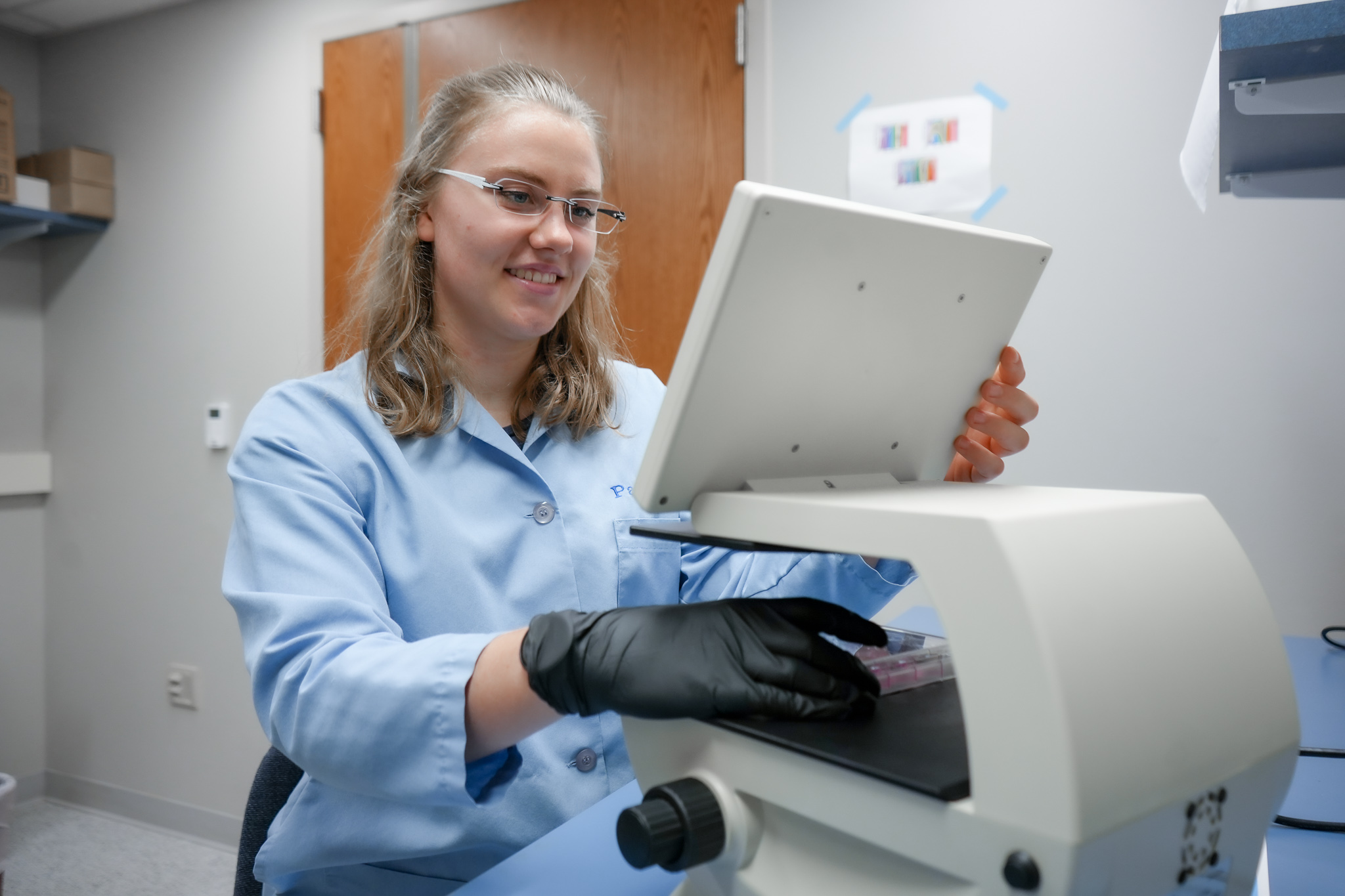 Lotta Truyen holds a tray of pink fluid samples underneath a processing machine