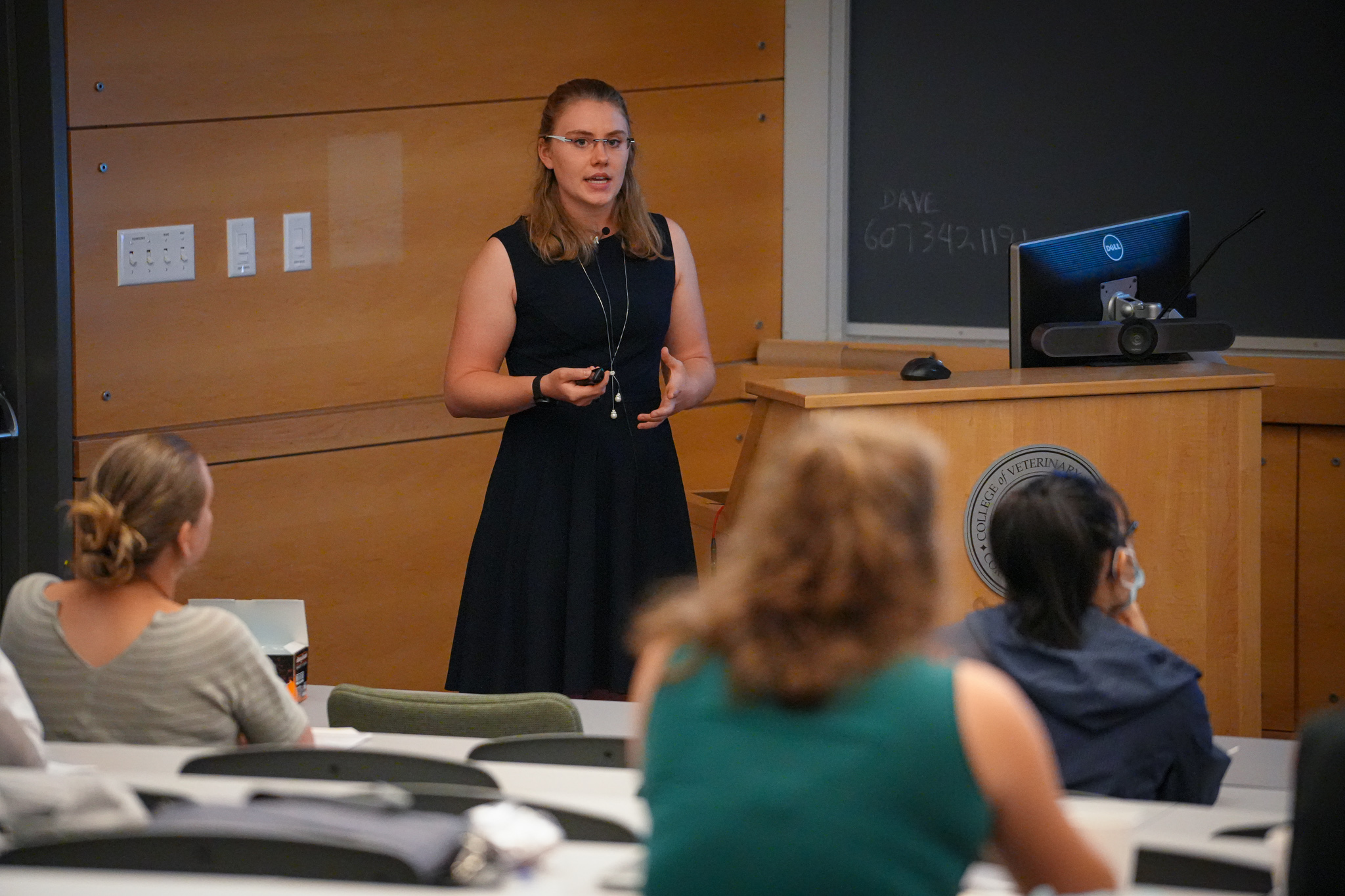 Lotta Truyen stands near a podium and talks to a her peers in a lecture hall