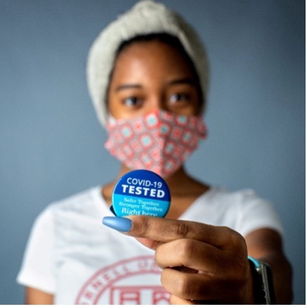 masked student holding Covid-19 tested sticker