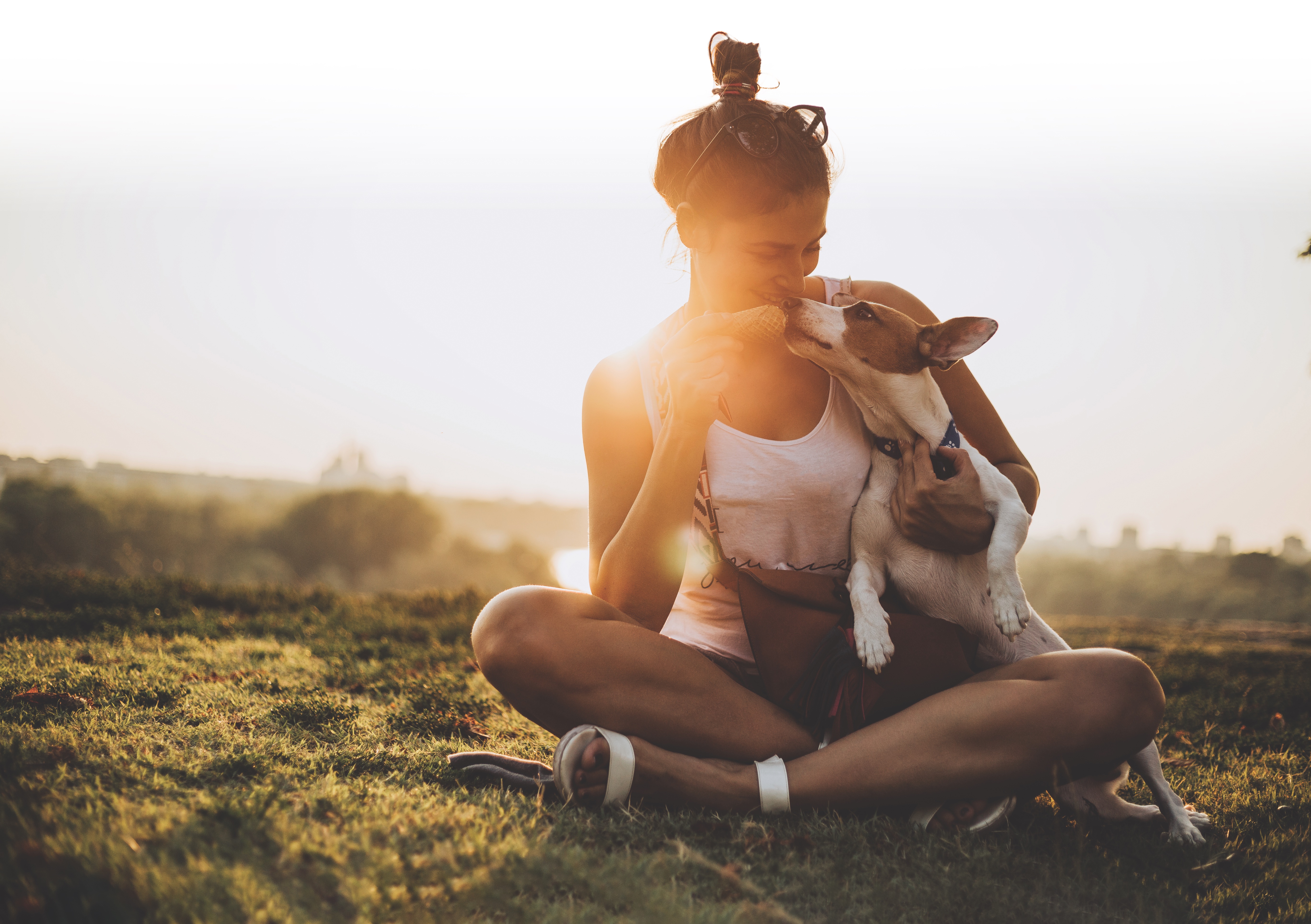 A woman sits in the grass with a dog in her lap