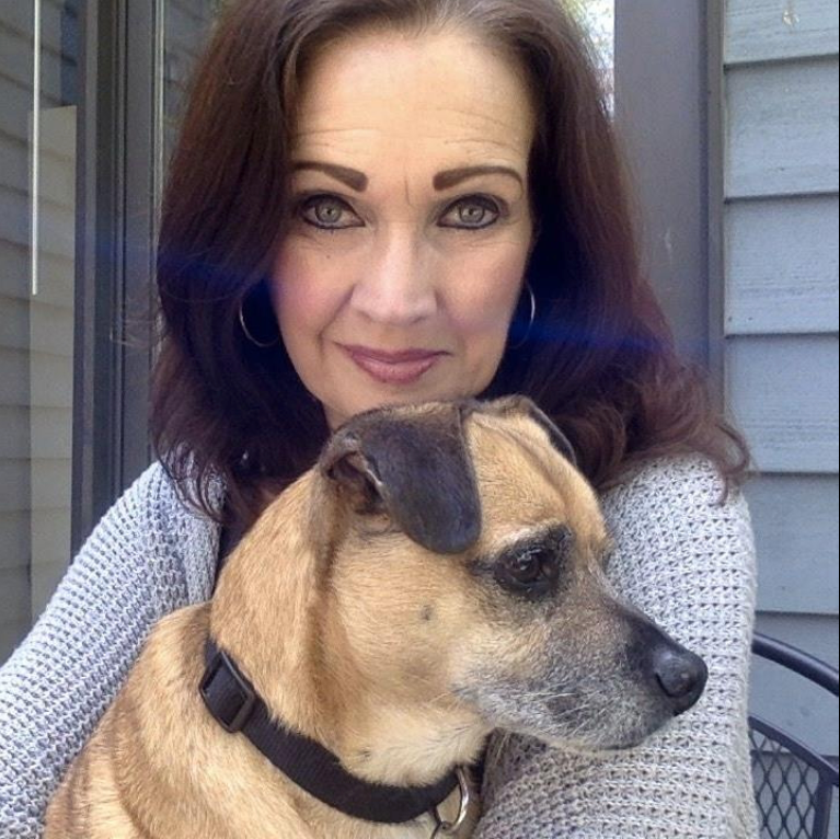 Susan Engelmore, a woman with dark brown hair wearing a light purple shirt, holds Milo an elderly terrier mix, close to her chest