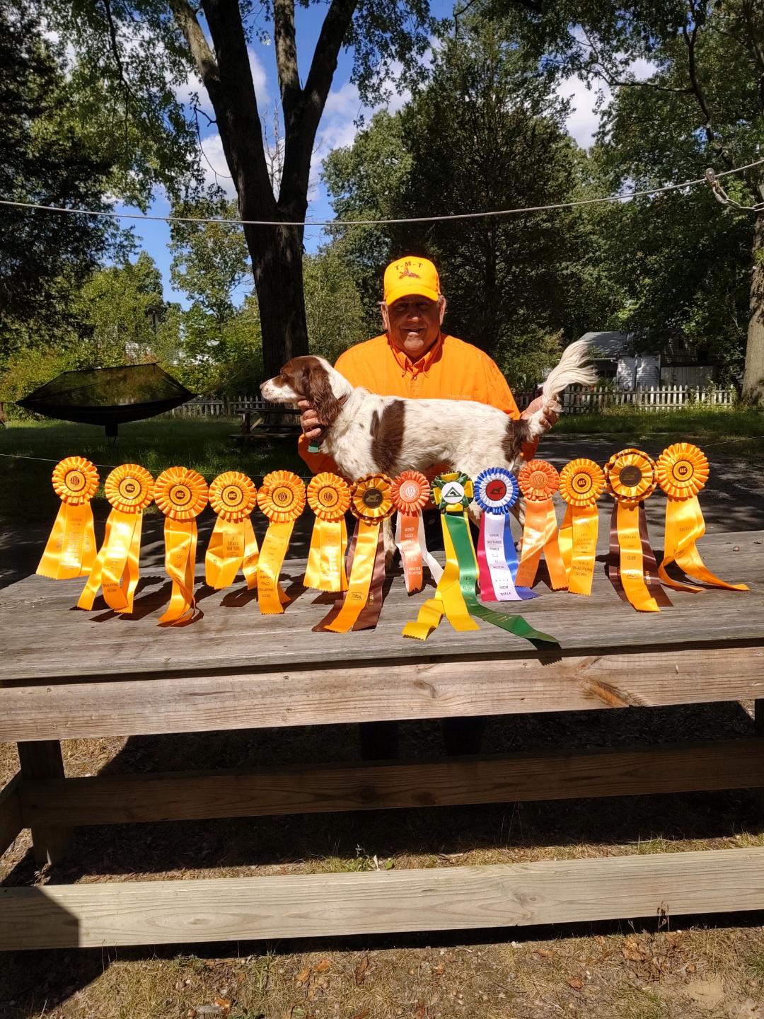 A man and his hunting dog stand behind a table full of awards