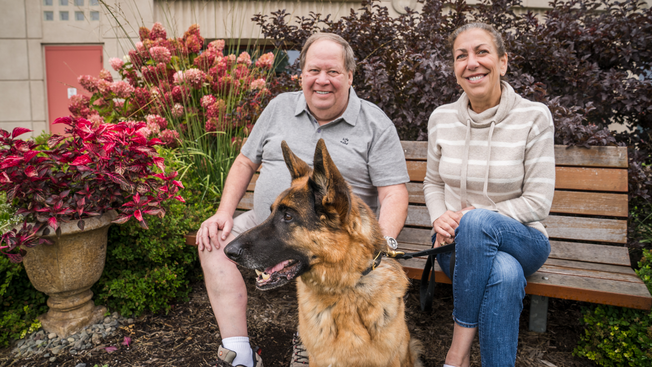 The Augusiewiczes with German shepherd Rex seated outside CUHA on a bench in front of flowers