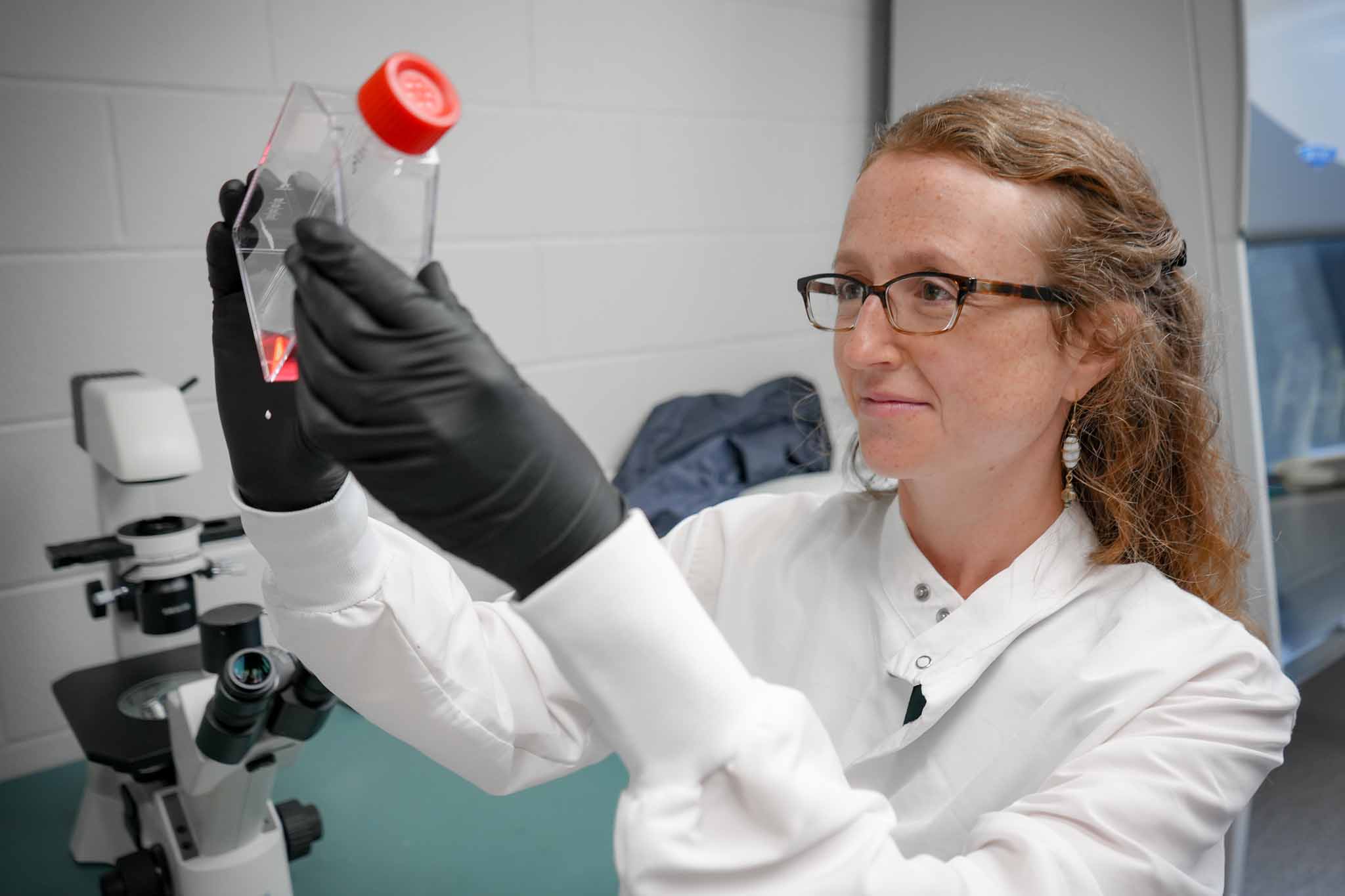 Dr. Sarah Caddy looks at a bottle with pink liquid in her lab.