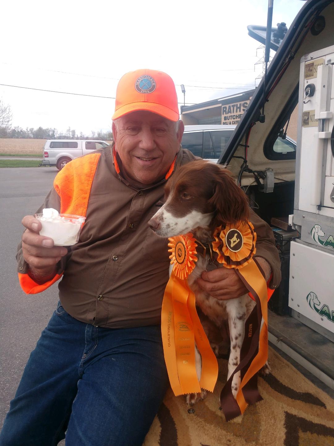 A man in hunting attire holds a pup cup for his eager dog