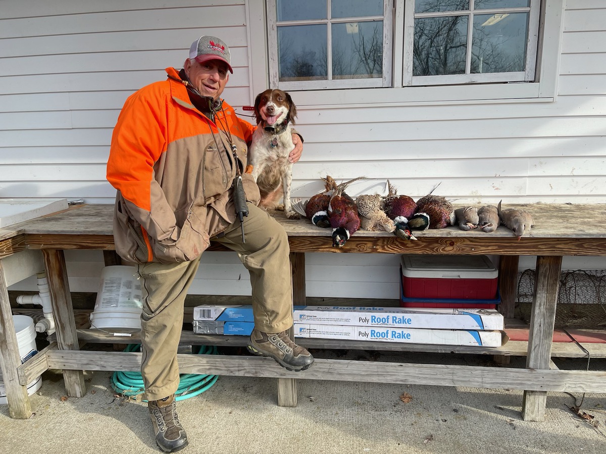 A man in hunting attire and his dog stand next to a row of harvested birds