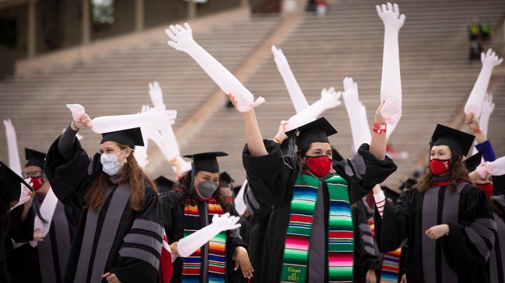 Veterinary students in cap and gown wave inflated palpation gloves at commencement