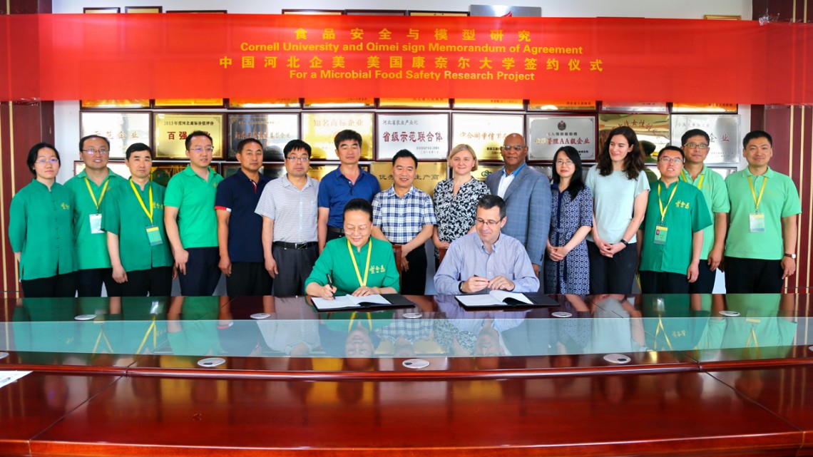 Yuqi Zhao, president of Qimei, left, and Martin Wiedmann, sign an agreement to collaborate on microbial food safety research while participants look on