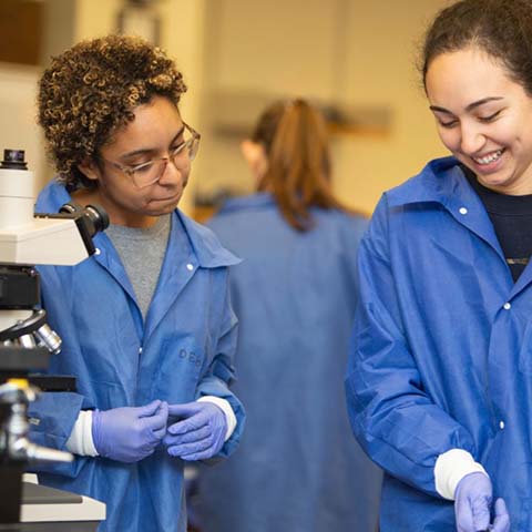 Two students in blue lab coats collaborating on something