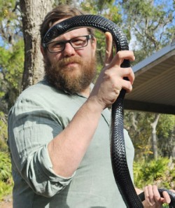 Robert "Oz" Ossiboff wearing a green shirt and holding a black snake.