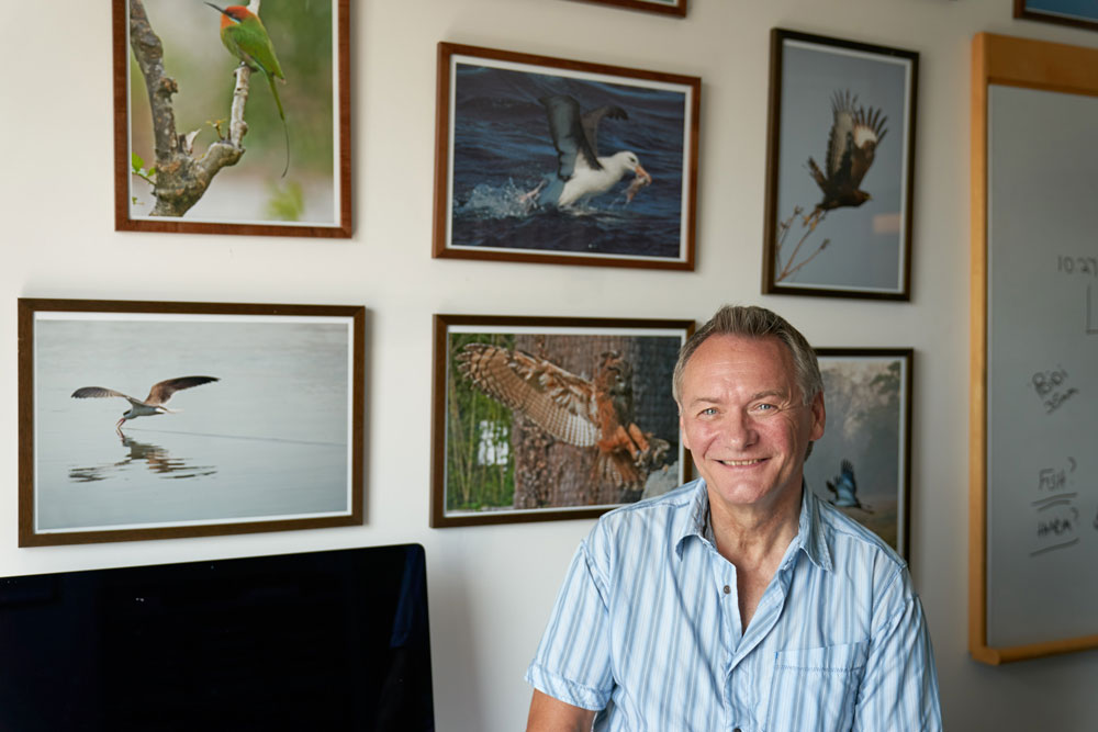 David Russell stands in front of a wall of his wildlife photographs