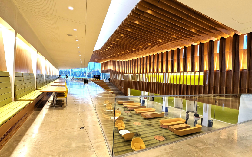 Modern lobby with wood paneling, green seating, and a lower lounge area with yellow chairs.