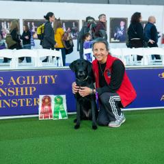 Alumna Liz Dole crouching next to her black Lab Chelsea at the agility competition