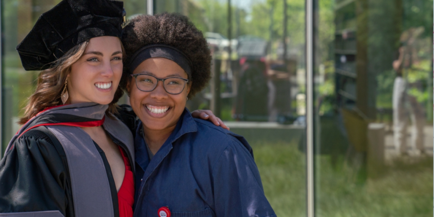 Two students in graduation gown smiling at the camera