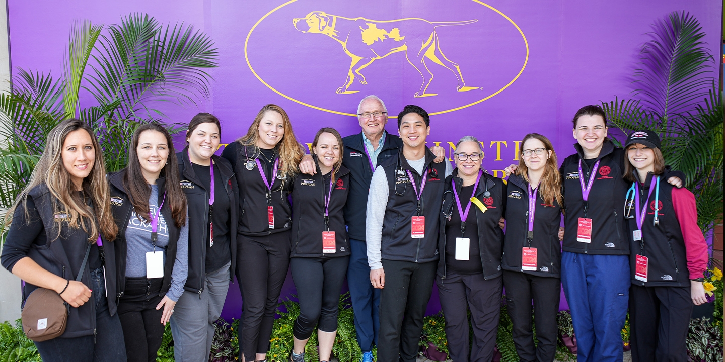 A group of people in black vests standing in front of a purple sign.
