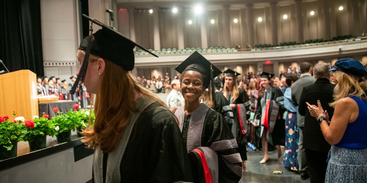 students smiling, walking in graduation gown