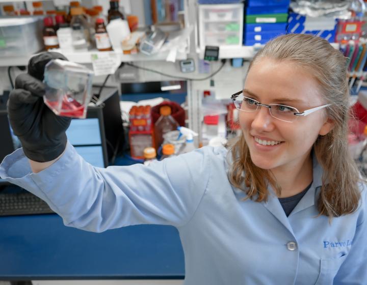 Lotta Truyen stands in Parrish Lab and holds up a flask with pink fluid