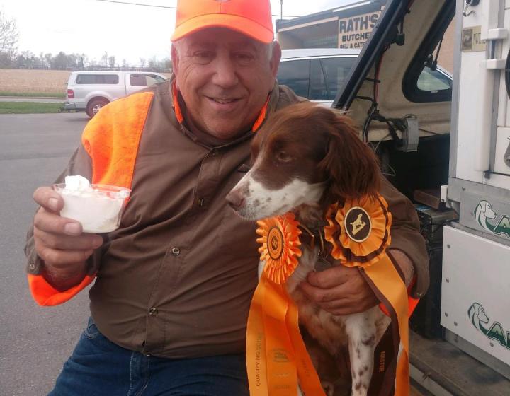 A man in hunting attire holds a pup cup for his eager dog