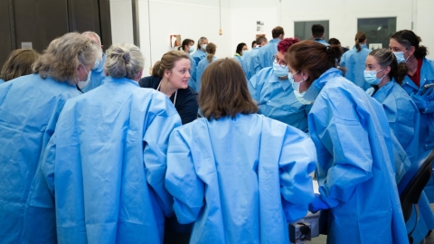 A group of veterinarians in smocks confer over a necropsy table