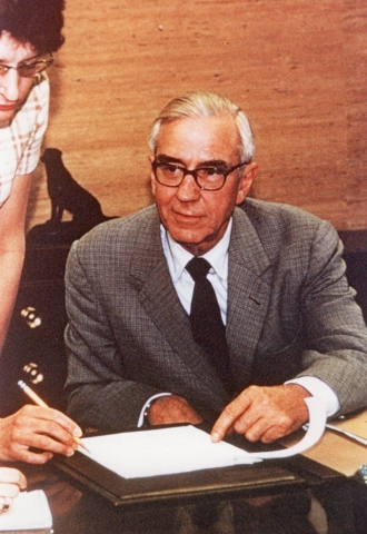 A photo of a man with glasses sitting at a desk.