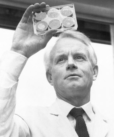 A white haired man does research while holding a clear container in the air. 