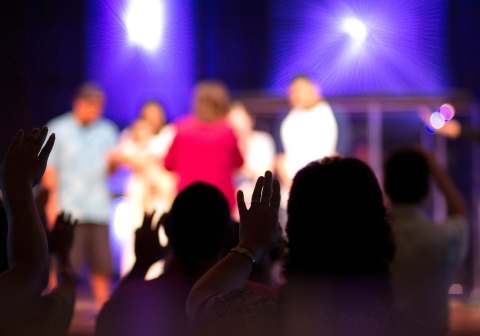 Silhouetted crowd with raised hands at a purple-lit event