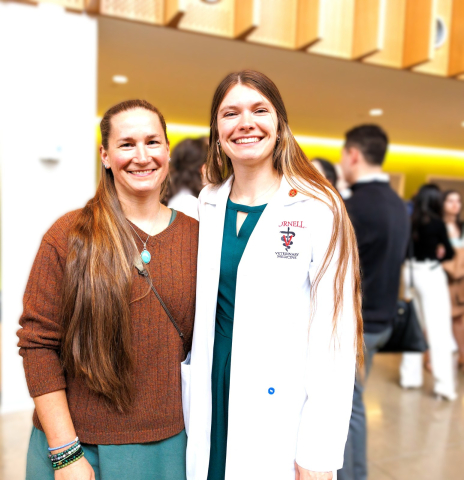 Two people posing together at an indoor event, one in a white coat.