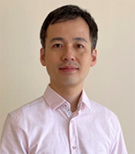 Satoshi Kimura in front of an off-white background wearing a light salmon-colored dress shirt.