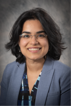Richa Sardana smiling, wearing an abstract blue blouse and a blue-gray blazer.