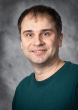Andrew Flyak in a gray background wearing a turquoise green shirt.