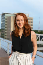 a red haired woman stands in front of a blue sky. 