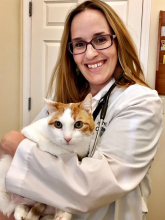 A woman in glasses and a lab coat poses with a white and orange cat