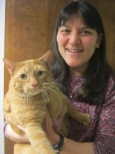 A woman with dark hair poses with an orange cat.