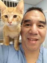 A man with dark hair poses with an orange cat on his shoulder. 