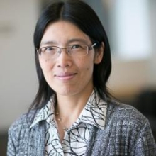 Fenghua Hu wearing thin-framed metallic glasses, a knitted gray blazer and a white collared shirt with Black-lined patterns.
